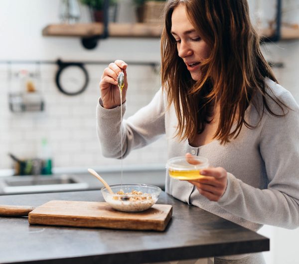 Young woman in the kitchen adds honey to granola