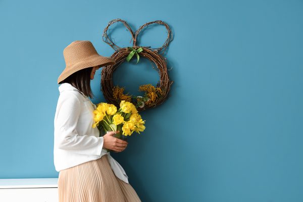 Easter Woman with stylish hat holding bouquet of tulips near color wall
