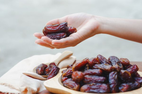Hand holding a date palm in a wooden cup It is a brown dried fruit that provides high energy and reduces fatigue. Muslims eat during fasting. (Ramadan month).